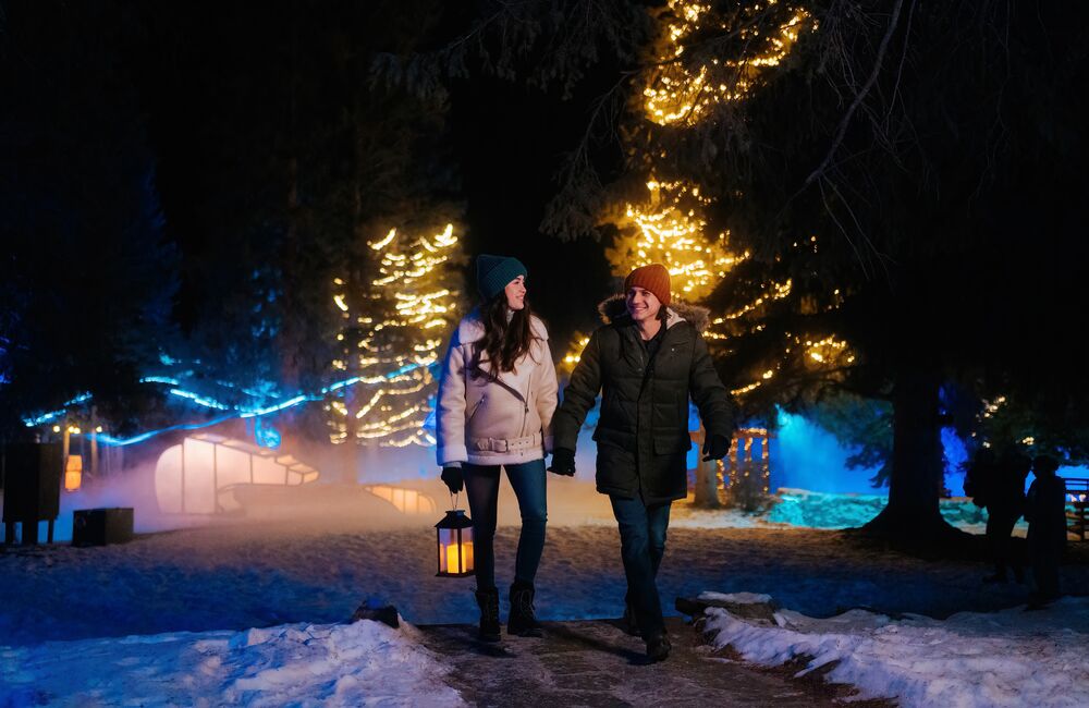 A couple walking through a lit up Cascade of Times Garden for In Search of Christmas Spirit in Banff